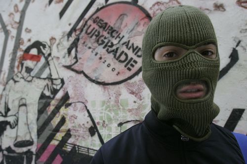 Автор на фоне своей старой работы; его лицо скрыто под маской - он не хочет, чтобы его лицо было известно; его ник Spy; ему 24 года; дизайн – его профессия, но street art – его при…